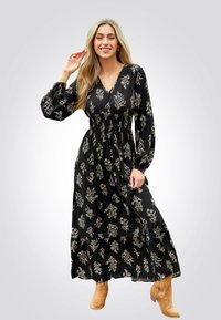Schwarzes Maxikleid mit floralen Mustern in Creme, langen Puffärmeln, smockierter Taille und gestuftem Rock. Tragen mit hellbraunen Ankle Boots.