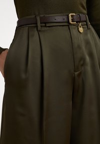 Olive green pleated trousers made of smooth fabric, paired with a dark brown leather belt featuring a gold buckle and a lock detail.