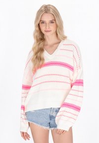 Maglione bianco lavorato a maglia con motivi a righe rosa, scollatura a V e vestibilità ampia. Abbinato a pantaloni shorts in denim, che mettono in evidenza un look estivo casual.
