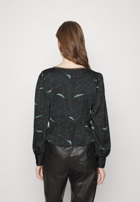 Svart blus med ett mönster av gröna blad, elastisk midja och rund halsringning med spetskant. Långa ärmar med rynkade manschetter.