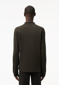 Polo a maniche lunghe di colore verde oliva scuro, con colletto e polsini aderenti. Tessuto liscio, cuciture minime e un design posteriore pulito.