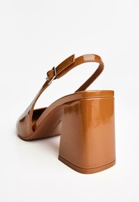Tan patenttaitoisten slingback-korkokenkien laaja lohkokorko, säädettävä hihna ja sileä pinta. Rentoa ja modernia muotoilua.