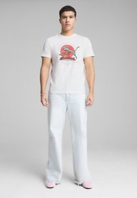 Camiseta blanca de algodón con estampado gráfico que presenta un animal colorido y texto. Combinada con unos jeans holgados de color azul claro y zapatillas rosas sin cordones.