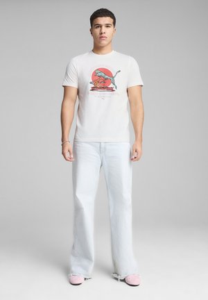 Camiseta blanca de algodón con estampado gráfico que presenta un animal colorido y texto. Combinada con unos jeans holgados de color azul claro y zapatillas rosas sin cordones.