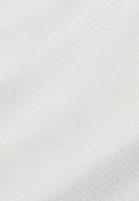 Gros plan sur un tissu blanc avec une texture tissée subtile et des plis doux créant des ombres délicates.