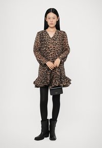 Leopardmønstrete kjole med volangkant, lange ermer, V-hals, lett stoff; kombinert med svarte ankelstøvletter og liten svart håndveske.