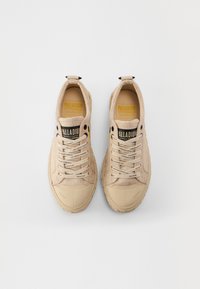 Beige sneakers with textured fabric upper, round toe, and stitched accents. Features flat laces and a padded tongue with logo.