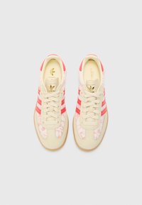 Sneaker beige con strisce rosse, tomaia floreale testurizzata e suola in gomma color beige. Lacci e branding in oro sulla linguetta.