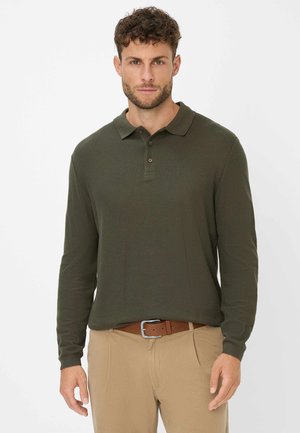 Dunkelgrünes langärmliges Poloshirt mit Kragen, einer Knopfleiste mit drei Knöpfen und gerippten Manschetten, kombiniert mit hellbeigen Hosen und einem braunen Gürtel.