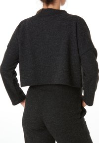 Pull noir cropped en maille texturée, avec un col haut et des épaules tombantes, assorti à un pantalon noir taille haute.