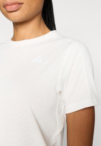 Λευκό κοντομάνικο μπλουζάκι κατασκευασμένο από απαλό ύφασμα, με μικρό ανάγλυφο λογότυπο σε σχήμα τρίγωνου στην αριστερή πλευρά και επίπεδα ραφές για άνεση.