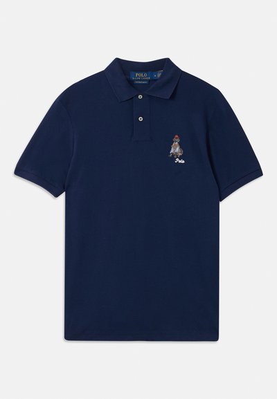 Polaire de algodão azul-marinho com uma pala de três botões e logotipo bordado de uma personagem com um chapéu vermelho no lado esquerdo do peito.