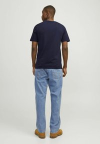 Camiseta de algodón azul marino con cuello redondo, mangas cortas y un corte relajado, combinada con jeans de mezclilla azul claro.