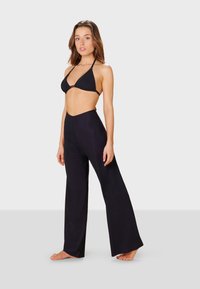 Svart triangulär bikiniöverdel i kombination med högmidjade, vida svarta byxor. Slät textur med minimal hårdvara och sömlös design.