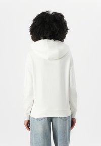 Witte hoodie met een trekkoord in de capuchon, zachte stof en geribbelde manchetten. Gecombineerd met lichtblauwe wijd uitlopende jeans. Schoon ontwerp, geen zichtbare logo's.