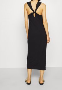 Černé maxi šaty bez rukávů s překrouceným detailem na zádech, obsahující klíčovou výřez a minimalistický design, vyrobené z měkké tkaniny.