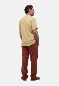 Chemise jaune à manches courtes avec un ourlet arrondi, assortie à un pantalon ample couleur rouille. Portée avec des chaussures à enfiler et les mains dans les poches.
