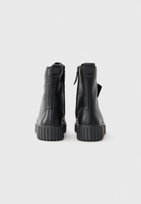 Bottines en cuir noir avec une semelle en caoutchouc texturée et une fermeture éclair à l'arrière. Présentent une finition lisse et une languette au dos pour un enfilage facile.