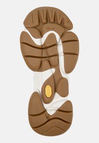 Braune und weiße Gummisohle eines Schuhs mit definierten Rillen, Kreis- und Wellenmustern sowie einem gelben Vibram-Logo. Strukturierte Oberfläche für besseren Halt.