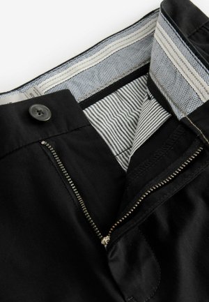 Mustadest puuvillast pükstest on lõikega lukuga ja nööbiga sulgemine. Vööosa sees on mustriga vooder, kus on triibud ja tekstuurilised aktsendid.