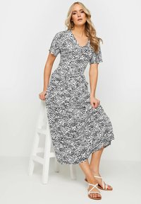 Schwarz-weiße gemusterte Midi-Kleid mit kurzen Ärmeln und V-Ausschnitt. Hergestellt aus leichtem Stoff mit einer fließenden Silhouette. Betonte Taille.