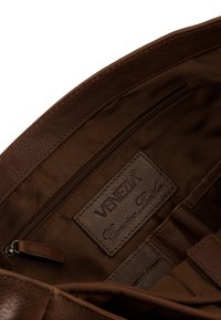 Interiér hnědé kožené tašky s kapsou na zip, texturovaným povrchem a koženou štítkem s nápisem "VENEZIA Genuine Leather."