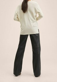 Top à manches longues de couleur crème clair associé à un pantalon en cuir noir à jambes larges, mettant en avant une coupe décontractée avec une texture lisse et un design minimaliste.