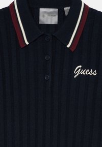 Tamsiai mėlynas raštuotas polo marškinėliai su raudono ir balto dryžių apykakle, trimis mygtukais ir išsiuvinėtu „Guess“ logotipu balta spalva. Medžiaga iš medvilnės mišinio.