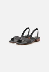 Sandali slingback in pelle nera con tacco basso, toe aperto e cinturini anteriori incrociati. Texture liscia con design minimalista.