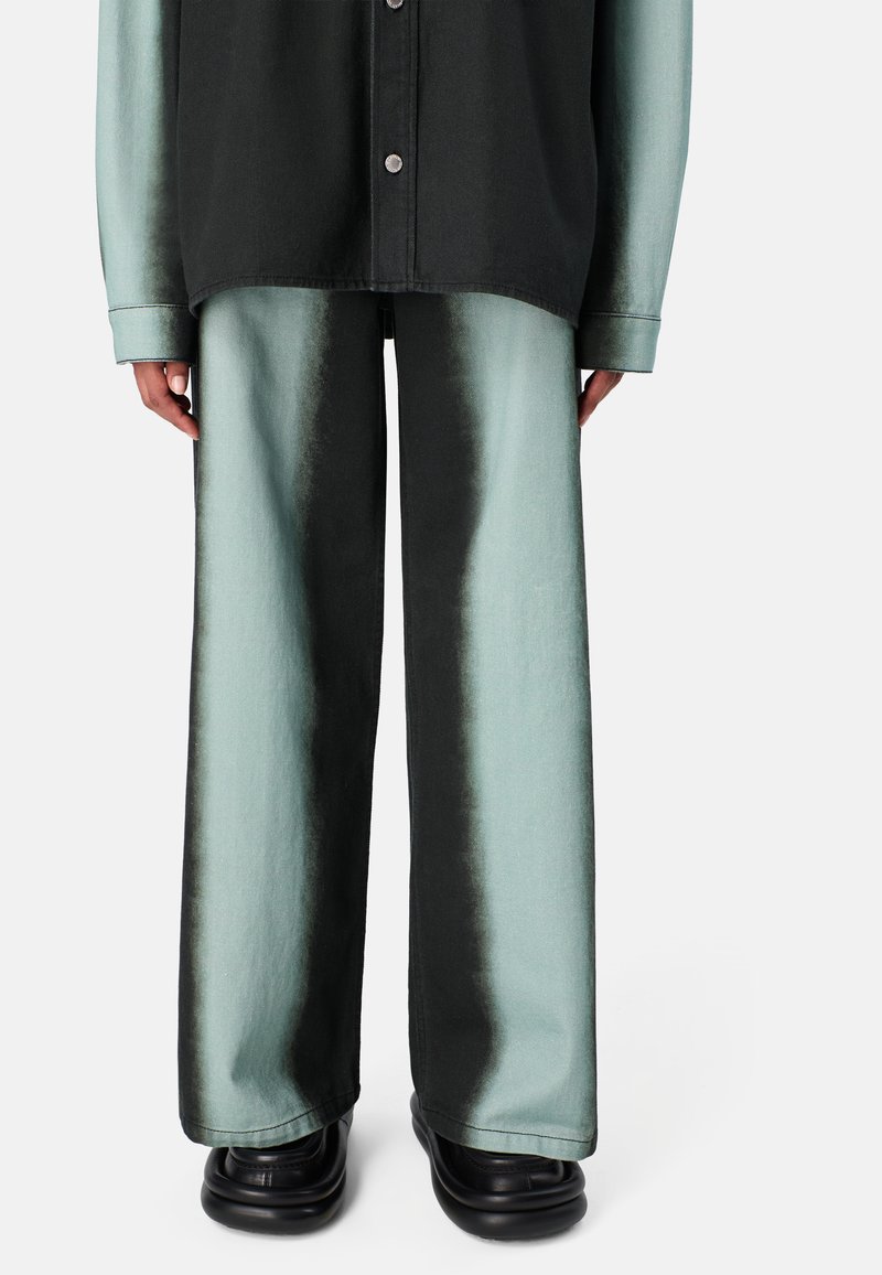 Kalhoty s širokými nohavicemi ve gradientu od smaragdově modré po černou se hladkou texturou, spárované s odpovídající volnou černou košilí na knoflíky.