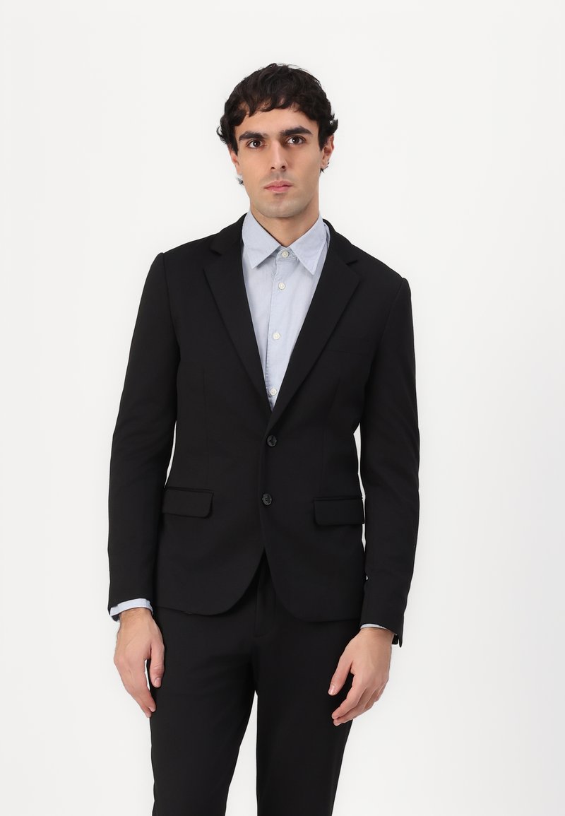 Schwarze taillierte Sakkjacke mit zwei Knöpfen, Reverskragen und vorderen Taschen, kombiniert mit einem hellblauen Hemd mit Knopfleiste.