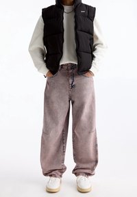 Černá prošívaná vesta přes světle šedou mikinu, doplněná světle růžovými volnými džínami. Součástí jsou velké kapsy a manžety, k tomu bílé tenisky.