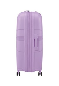 Valigia rigida di colore lavanda pastello, con strisce verticali testurizzate, doppie cerniere, maniglia laterale e quattro ruote girevoli nere.