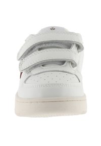 Baskets blanches avec trois bandes Velcro, boîte à orteils perforée et texture en cuir lisse. Semelle en caoutchouc avec une couleur d'accent subtile.