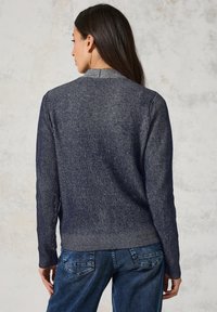 Marinblå ribbad tröja med en subtil textur, med hög halsringning och långa ärmar, kombinerad med blå denimjeans.