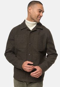 Chaqueta de mezcla de lana marrón con cuello de solapa, dos grandes bolsillos con solapa, cuatro botones y un acabado texturizado. Llevada sobre un cuello de cisne crema.