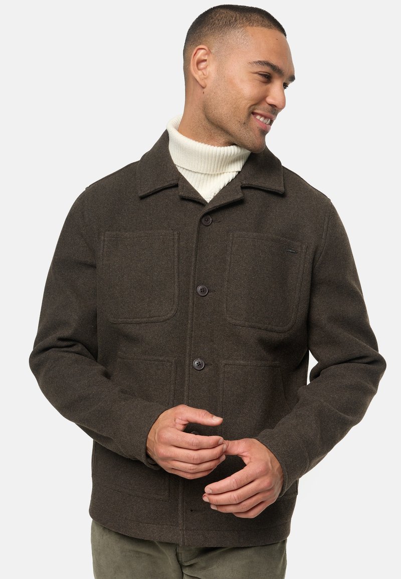 Chaqueta de mezcla de lana marrón con cuello de solapa, dos grandes bolsillos con solapa, cuatro botones y un acabado texturizado. Llevada sobre un cuello de cisne crema.