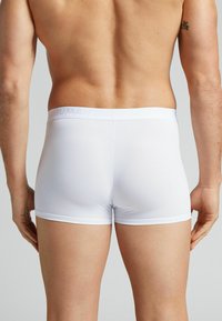 Boxers blancs en tissu lisse et extensible avec une ceinture douce portant un logo en relief, vus de l'arrière.