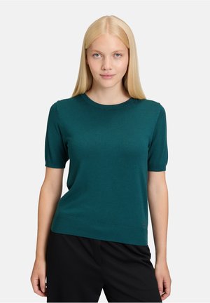 Teal trui met korte mouwen, ronde halslijn en geribbelde zoom. Zachte textuur met aansluitende mouwen, gecombineerd met zwarte pantalon.