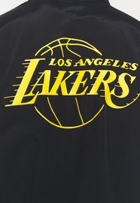 Schwarzer Stoff mit großem gelben "LOS ANGELES LAKERS"-Text und einer Basketballgrafik, mit fetter Typografie und glatter Textur.