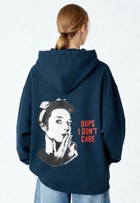 Felpa con cappuccio blu navy dalla vestibilità oversize. Presenta una stampa grafica sul retro con il volto di una donna e la scritta "OOPS I DON'T CARE" in rosso.