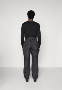 Camisa preta de mangas compridas combinada com calças cinzentas largas, com um tecido texturado e dois bolsos traseiros.