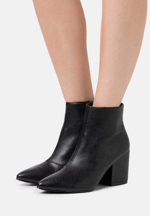 Bottines en simili cuir noir avec une finition texturée, un bout pointu et un talon épais. Le design présente une silhouette épurée et minimaliste.