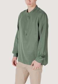 Camicia a maniche lunghe verde in tessuto leggero con colletto alto, patta con bottoni e vestibilità rilassata. Caratterizzata da polsini con bottoni e aperture laterali.