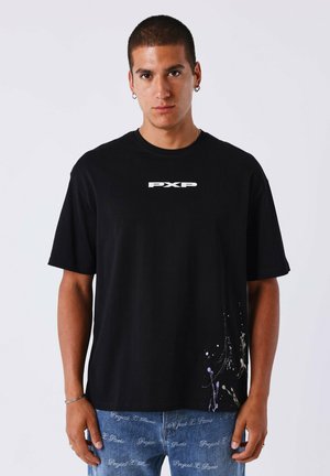 Zwarte katoenen t-shirt met korte mouwen, met een wit "PXP" logo op de borst en een kleurrijk verfspetterontwerp aan de onderrand.