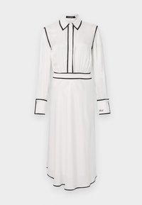 Robe chemise blanche avec bordures noires, col chemise, manches longues, fermeture à boutons sur le devant et une silhouette en A. Présente des détails brodés sur la manche.