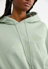 Felpa verde menta realizzata in tessuto morbido, con un grande logo Nike sottile in una tonalità più chiara, dotata di lacci e di un cappuccio ampio.