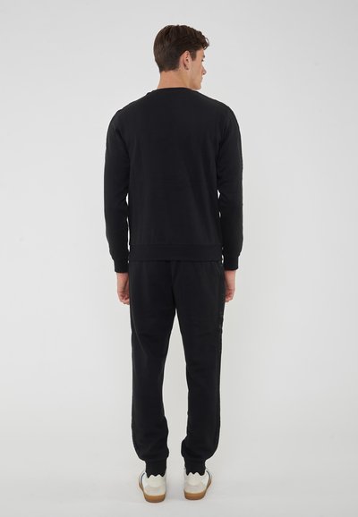 Completo di felpa e pantaloni della tuta neri, realizzato in materiale morbido. Presenta un collo a giro, polsini e orlo a costine, con una vestibilità comoda.