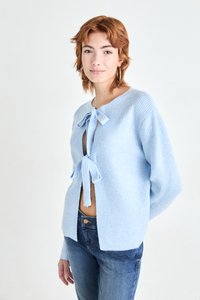 Ljusblå cardigan i ribbat tyg, med knytning i halsen och sidslitsar, parat med åtsittande blå jeans.