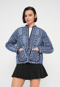 Μπουφάν μπλε με σχέδια λουλουδιών, κλείσιμο με φερμουάρ και δύο εμπρόσθιες τσέπες. Μαλακό ύφασμα με μακριά μανίκια και στρογγυλό γιακά.